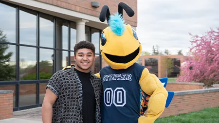 Stinger mascot posing with student outside.