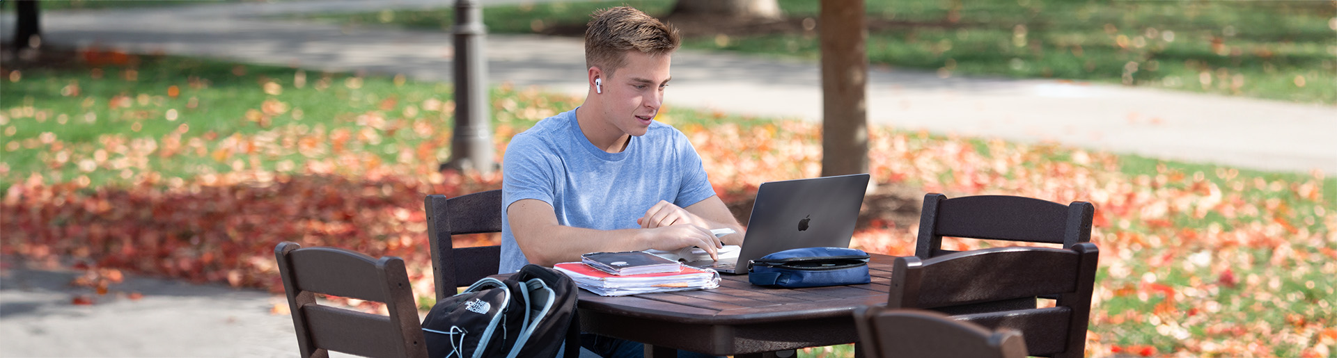 Student attending class online while sitting at an outside table.