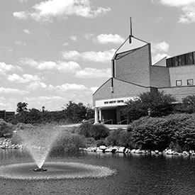 Exterior view across Cedar Lake with a fountain in the foreground and the Dixon Ministry Center building behind.