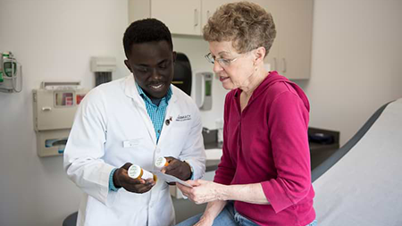 male Pharmacy student handing prescription bottles to elderly female patient in a clinic setting