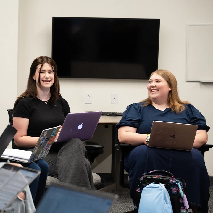 Two students with laptops talking and laughing.