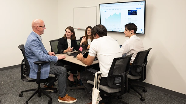 Students talking with a professor in a classroom.