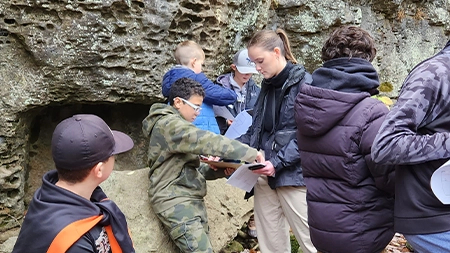 Middle school students with teacher holding worksheets outdoors.