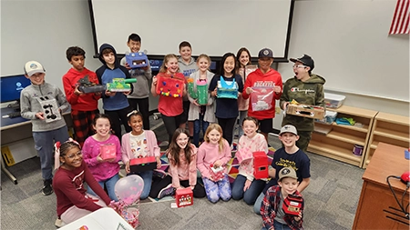 Group of middle school students smiling in classroom holding Valentine's Day gifts.