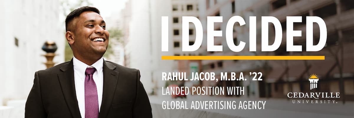 Photo of man in a suit and tie with buildings in the background. I Decided is in a large bold font. Text overlay states Rahul Jacob, M.B.A. '22, Landed position with global advertising agency. Cedarville University logo