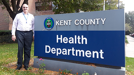 Cedarville alumnus Gary Osantowski standing next to Kent County, Michigan Health Department sign. 