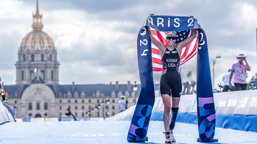 Grace Norman at Paris Paralympics crossing triathlon finish line draped in American flag 858