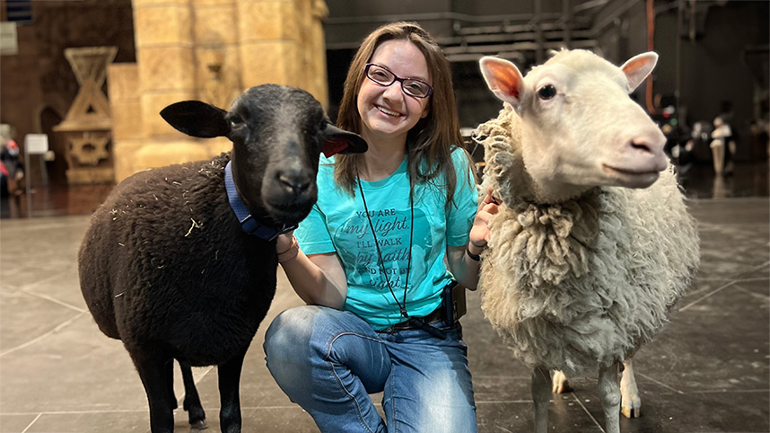 Abigail King on theatre stage smiling next to two sheep.