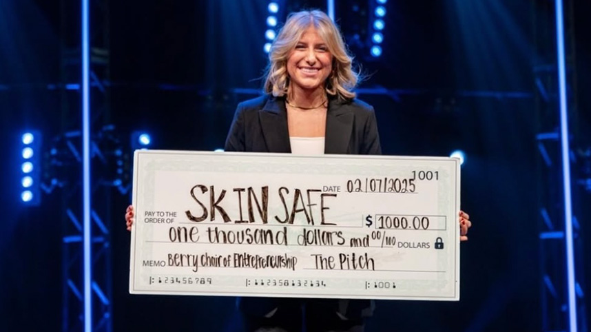 Alex Simons smiling onstage holding large check addressed to Skin Safe.