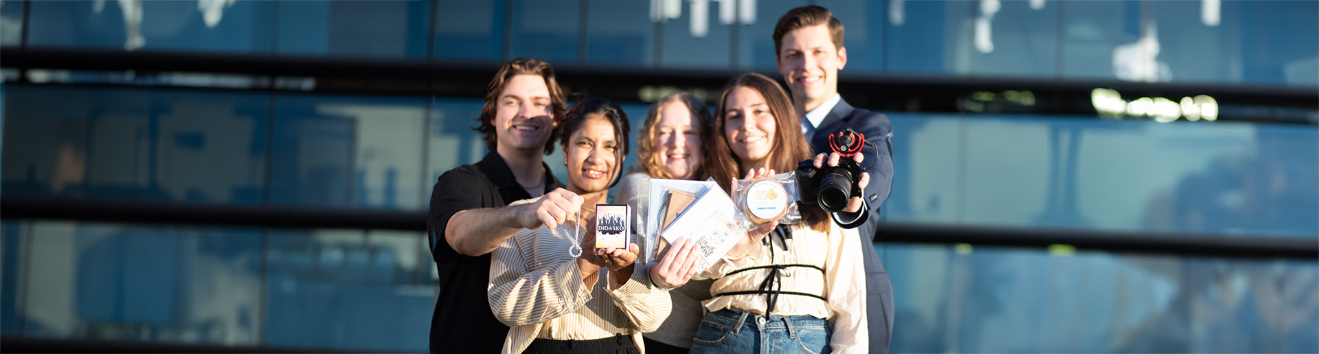 Five students smiling and holding up products from their entrepreneurial businesses.