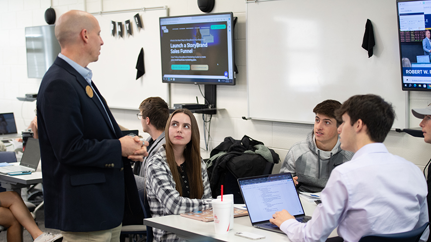 Professor talking with four students working at a table during class.