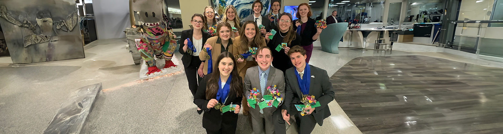 Cedarville University&#39;s forensics team smiling holding medals with blue ribbons.