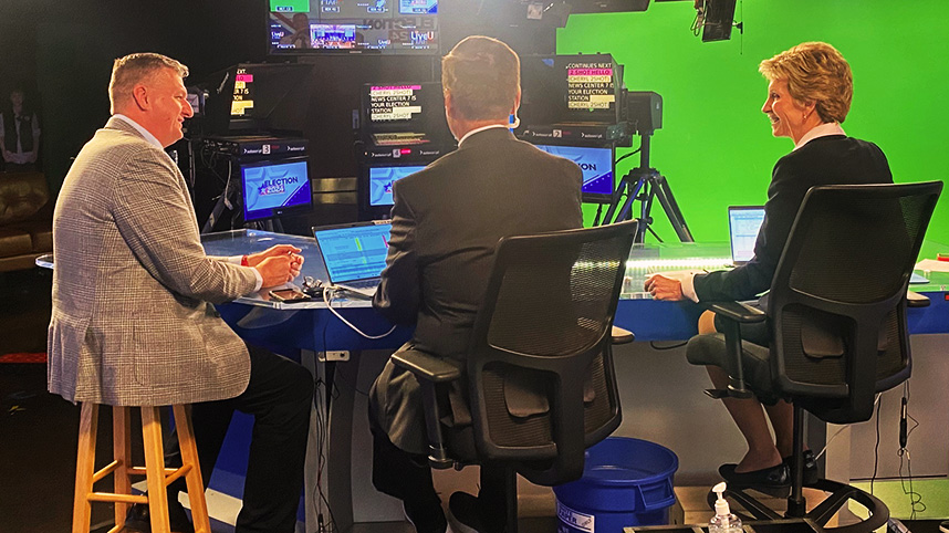 Dr. Mark Caleb Smith sitting behind news desk with news anchor giving an interview.