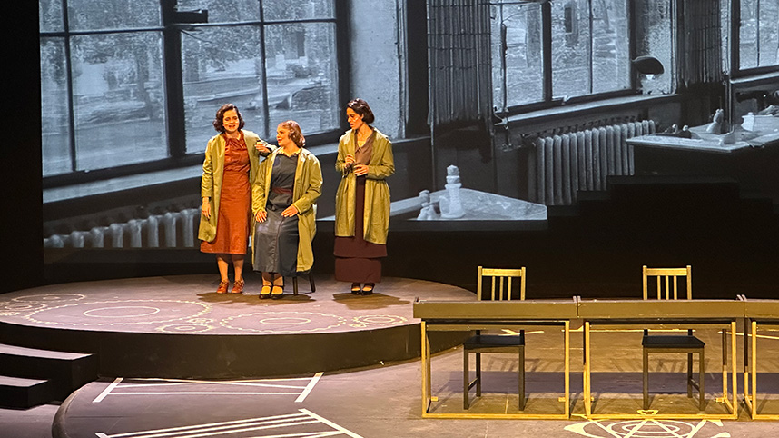 Three students in green lab coats talking and acting onstage.