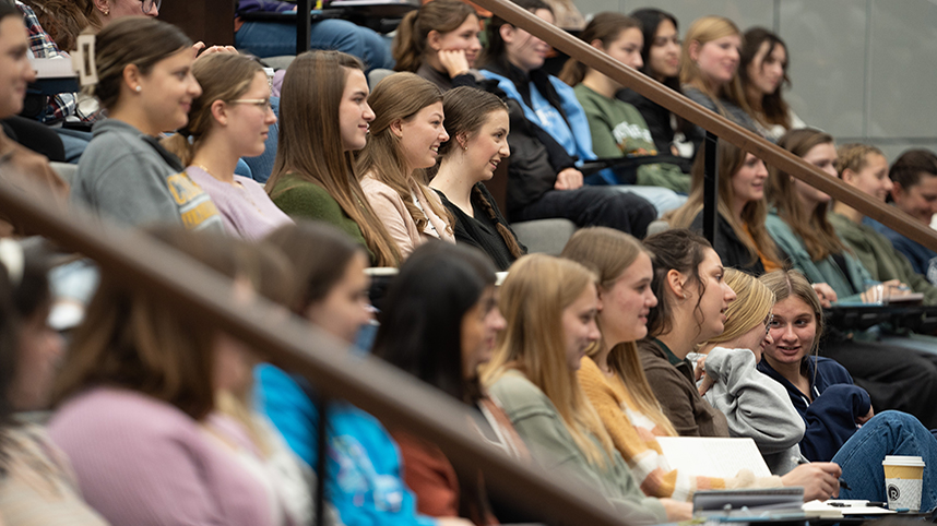 Smiling students sitting in class in the Scharnberg Business and Communication Center auditorium.