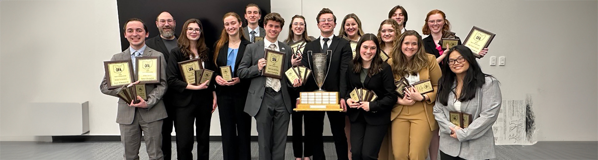 Cedarville&#39;s winning speech and debate team smiling holding plaques and a trophy.