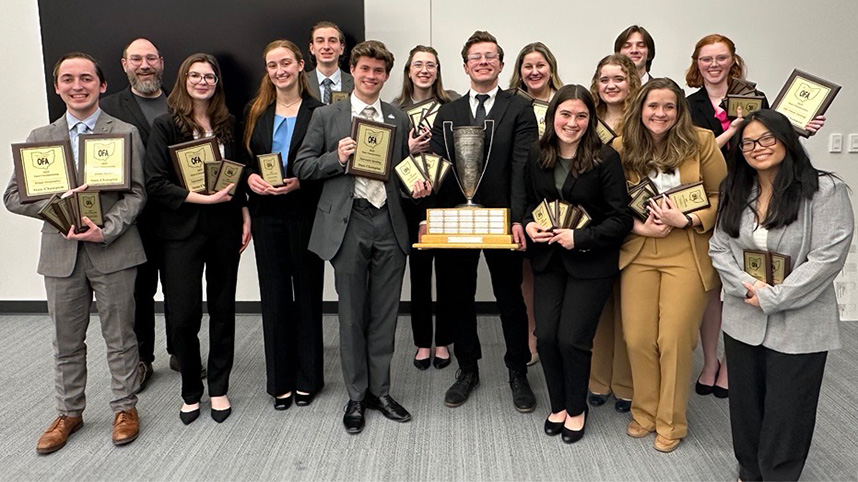 Cedarville's winning speech and debate team smiling holding plaques and a trophy.