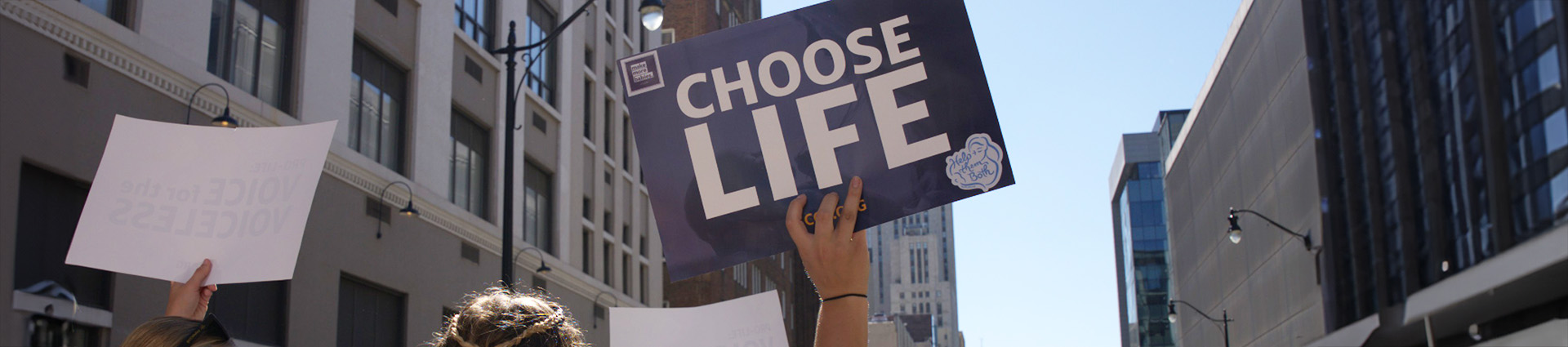 Woman marching on city street holding a sign that says choose life.
