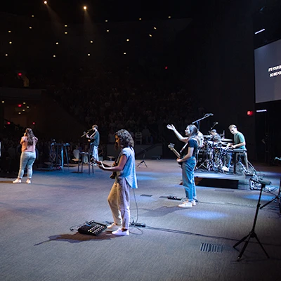 Band playing instruments onstage and looking out towards crowd.