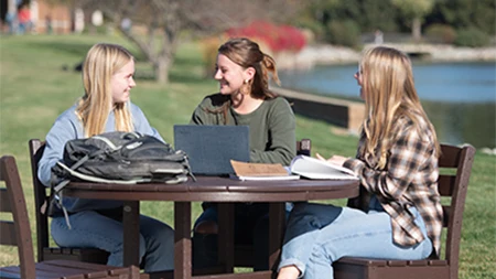 Three female students studying together and laughing at table outside.