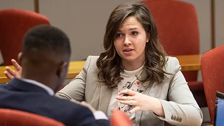 Graduate student in professional attire engaged in a one-on-one conversation during in a classroom.