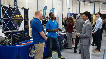 Students and recruiters engage in conversation at a Cedarville University career fair held in a campus gymnasium.
