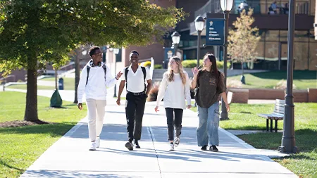 Four students with backpacks walking and talking along sidewalk.