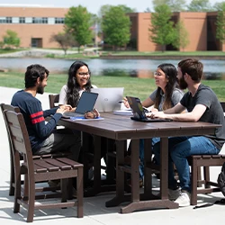 Group of four friends laughing and studying together at a table on the lakeside patio.