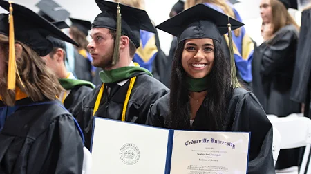 Graduate smiling with diploma at graduation ceremony.