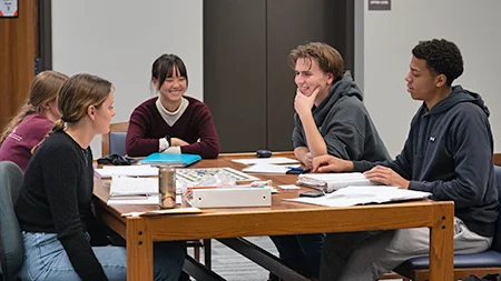 Five friends studying together at table in library.