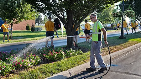 A man watering colorful flowers using a green hose.