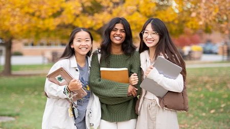 Three friends smiling and holding schoolbooks.