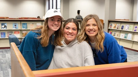 Three students smiling together while studying in library.