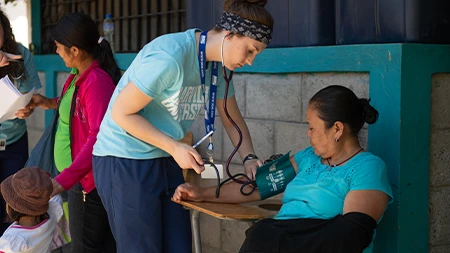 Nursing student taking woman's blood pressure outside.