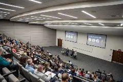 An auditorium packed with people in chairs, all focused on the stage, creating a lively and engaging environment