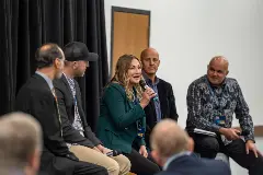 A woman leads a panel discussion, engaging with an attentive audience of diverse individuals.