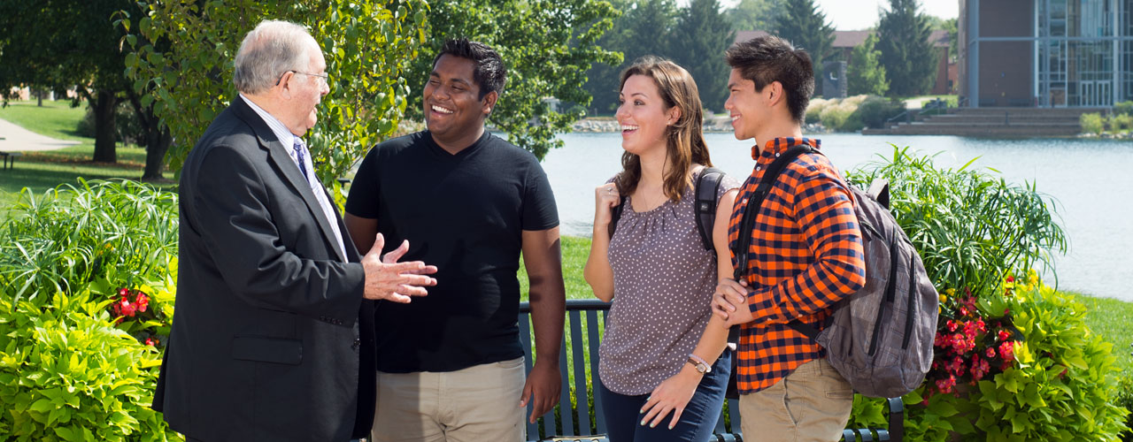 A diverse group of students talk to a professor on Cedarville's beautiful campus
