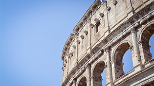 Partial view of the Colosseum in Rome, Italy, featuring its ancient arches against a clear blue sky.