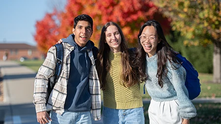 Three students smiling with arms around each other.