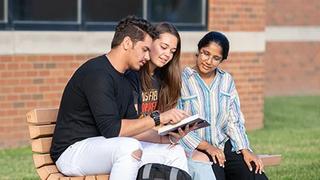 Three students sitting on bench reading Bible.