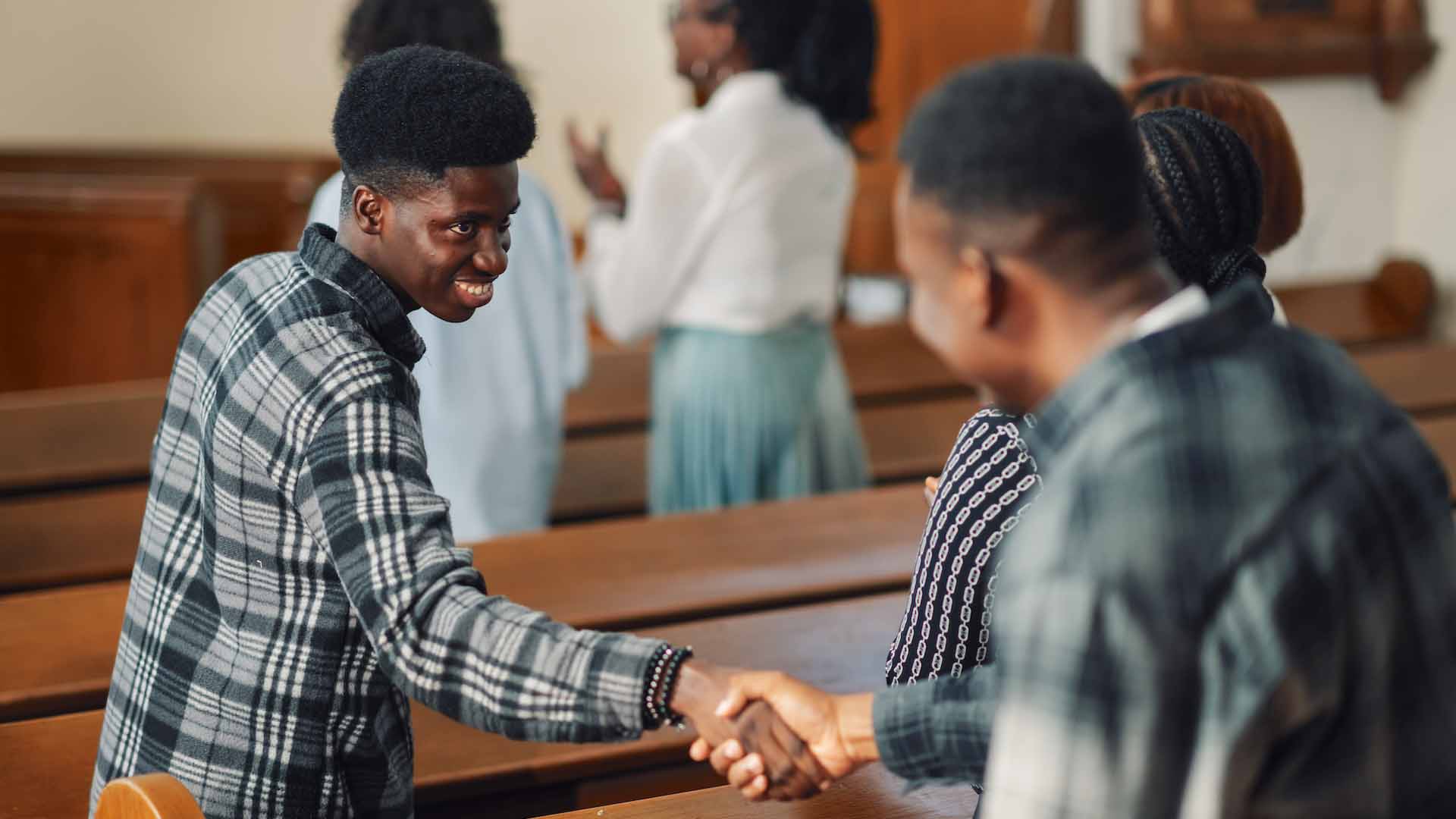 Man shaking hand of man behind him in church pews.