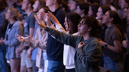 Students raising hands in worship during chapel.